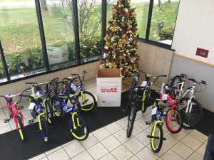 11 Bikes are posed in the corner of the main lobby for the DIA Toys for Tots Charity event supported by Trans-Overseas Corporation. In the center is a Toys for Tots donation box and behind it, a brightly lit and ornately decorated Christmas Tree.